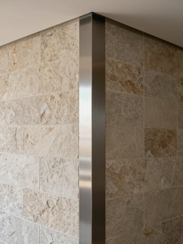 Material junction detail at a completed interior wall — stone tile meeting a brushed steel reveal at a corridor corner, even diffused daylight from above, visible grout lines and precise mitre cut, no furnishings or people