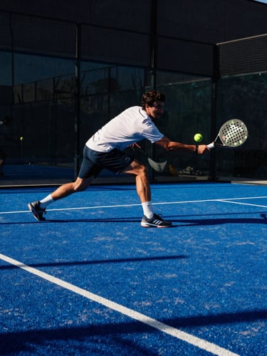 Dynamic low-angle action shot of a padel player mid-swing on a blue court, high-contrast Texas sunlight, sharp shadows, electric blue accents, wide-angle action lens, 35mm film grain.