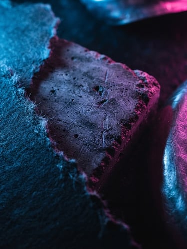 Extreme close-up of a physical brand mockup with raw textures, illuminated by electric blue and hot pink neon lights, dramatic shadows, gritty flash photography.