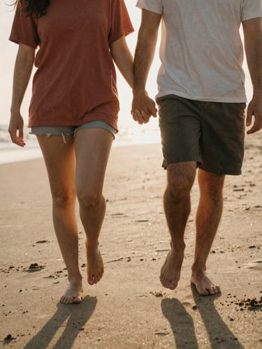 Intimate medium portrait of a couple walking barefoot on a sandy beach, holding hands, warm backlighting from the setting sun, soft natural flares, candid interaction, 35mm film style.