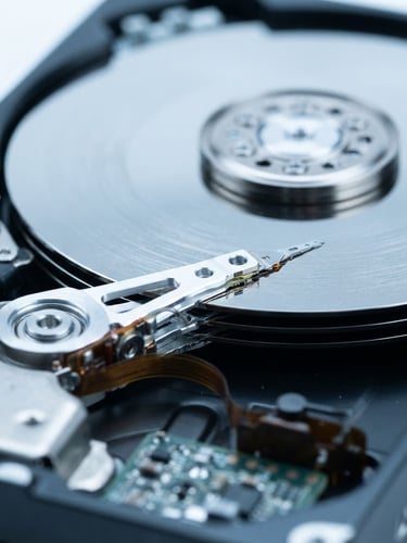 Clinical macro photography of an exposed hard drive platter under bright sterile white light, cool metallic tones, sharp focus, shallow depth of field