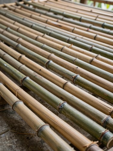 Close-up ground-level view inside a bamboo drying shed in West Java, cut bamboo culms laid flat in tight rows, natural side-light raking across the surface texture, concrete floor partially visible, no people