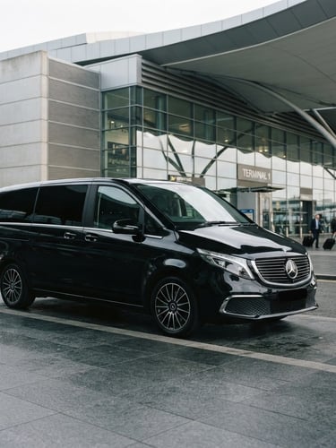 Elegant editorial photography of a pristine black Mercedes-Benz V-Class parked in front of a modern airport terminal, soft overcast daylight, clean architectural lines, 35mm