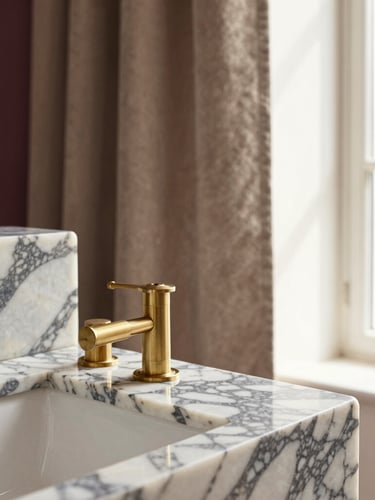 Close-up of rich interior materials, polished Calacatta marble with deep grey veining, brushed brass fixtures, and soft taupe velvet fabric under warm natural window light.