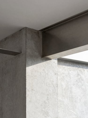Close-up of a meticulously crafted raw material junction in a luxury residential interior, showing poured concrete meeting brushed steel under sharp, natural light, emphasizing texture and precision