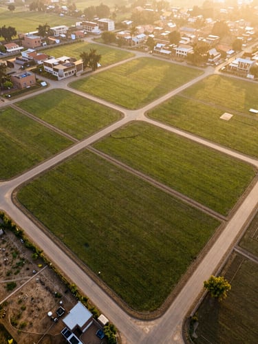 Wide environmental drone shot of cleared residential plots in Phagwara under warm golden hour sunlight, showing clean geometric boundaries and road connectivity