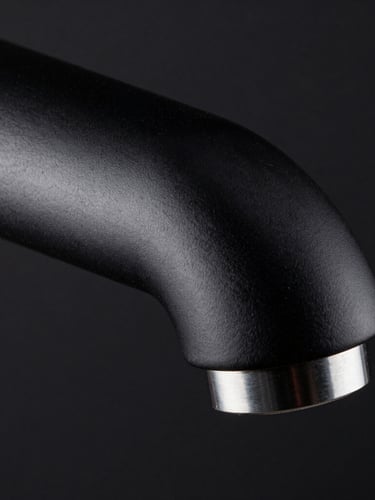 Extreme macro shot of a monolithic matte black faucet spout, high-contrast side-lighting catching the sharp metallic edge, dark background.
