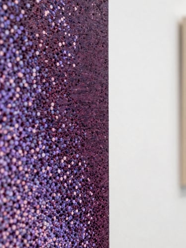 Extreme close-up of a finished pointillist canvas edge under diffuse north-facing studio light, dense dot clusters in deep aubergine and soft lavender visible at macro scale, white gallery wall behind, architectural calm