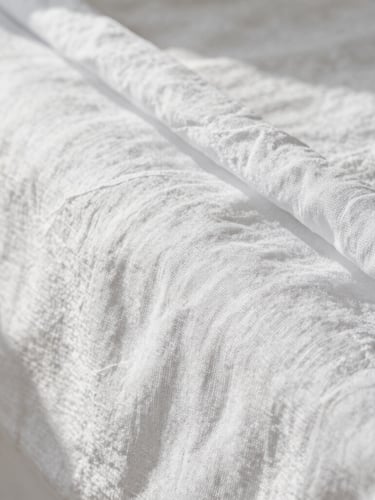 Macro shot of perfectly ironed white linen sheets, crisp textures with soft natural morning light, clean shadows, minimalist composition.