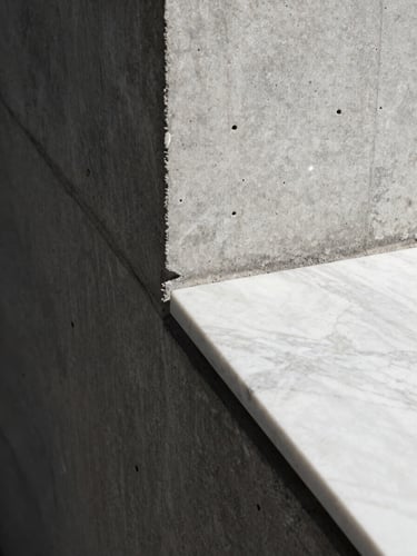 Tight geometric close-up of a raw concrete wall meeting a polished white marble slab, hard direct sunlight casting a razor-sharp shadow line diagonally across the frame.
