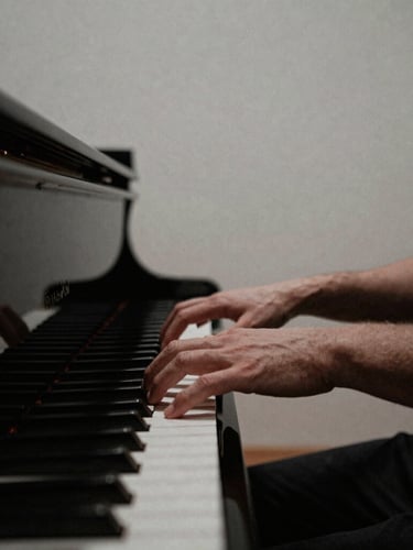 Hands of a musician gently playing a grand piano in a quiet, sunlit chapel, minimalist composition, deep muted tones, 35mm film grain