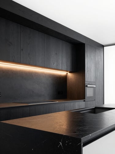 Sleek modern kitchen at twilight, linear LED profiles seamlessly embedded under dark oak cabinets, casting warm glare-free light onto a black marble countertop, architectural photography style.