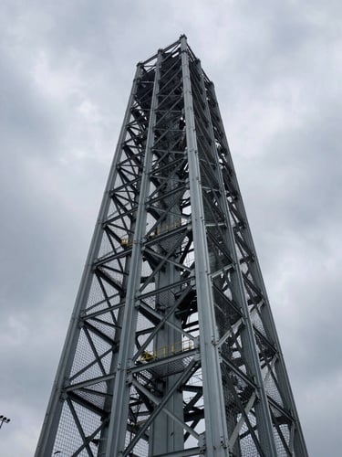 Low-angle perspective of a massive steel cage structure for a bridge pillar, dramatic overcast sky, raw industrial power.