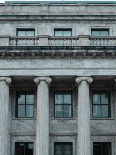 Architectural detail of a classic state treasury building facade, cool neutral daylight, desaturated corporate blue tones, 35mm