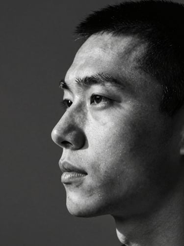 Close environmental portrait, photographer's face in three-quarter profile, directional north-light casting a precise shadow across one side, dark neutral studio background, high-contrast black and white, tight crop below chin