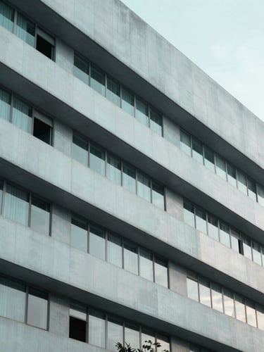 A sharp architectural close-up of a modern pharmaceutical research facility facade in Bangalore, desaturated teal and slate tones, cool diffused morning light.