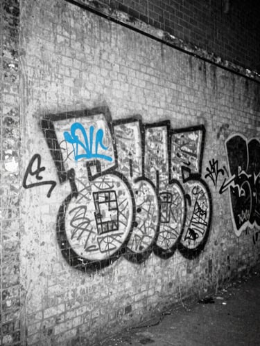 Harsh direct-flash black and white photograph of a concrete East London alleyway at night, electric blue graffiti tag on the brick wall, gritty 35mm film grain