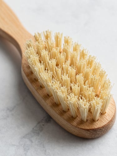 Overhead macro shot of a tactile beechwood scrub brush with stiff natural bristles resting on a light grey marble countertop, bright natural daylight, shallow depth of field