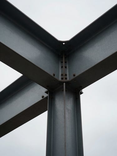 Dramatic low-angle shot of structural steel beams bolted together, high-contrast overcast sky, raw blasted steel texture.