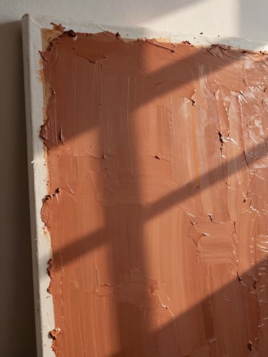 Close-up portrait-format shot of a large canvas leaning against a studio wall, warm afternoon light raking across thick oil pigment ridges, raw linen edges visible at the top, terracotta and earth tones dominating the composition