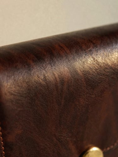 Macro close-up of detailed saddle stitching on a dark mahogany leather bag, warm natural light, soft shadows, 35mm film grain