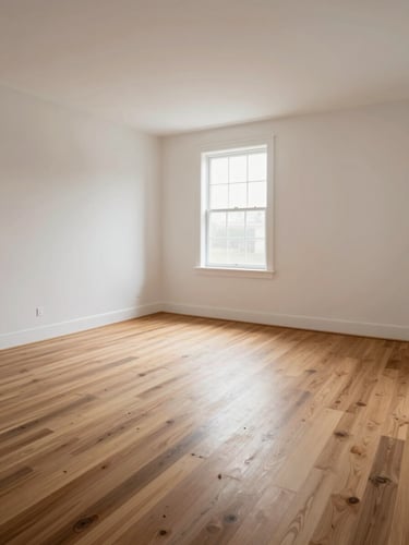 Wide establishing shot of a fully renovated interior — hardwood floors, clean plaster walls, north-facing window light casting even illumination across the room, no furniture, no staging, architectural detail at the baseboard transition visible