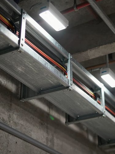 Close-up overhead study of a steel cable tray being installed in a technical ceiling, wiring bundles neatly routed, bright task lighting from above, raw concrete wall visible at the edge, industrial precision framing