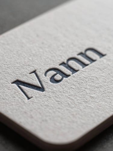 Extreme macro shot of a heavy textured paper business card with embossed typography, soft indirect daylight highlighting the physical paper grain and crisp edges.