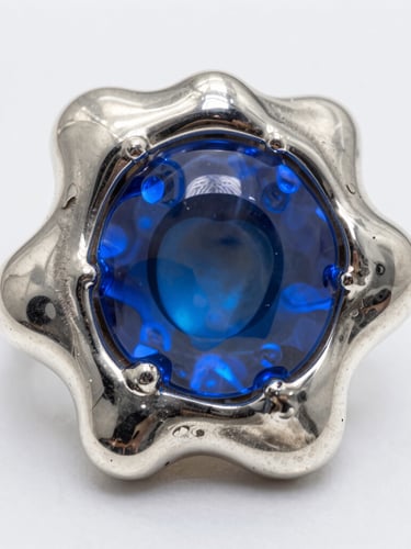 Macro shot of molten sterling silver solidifying into organic, fluid shapes, high contrast studio lighting, electric blue gel reflections, sharp metallic textures, 35mm