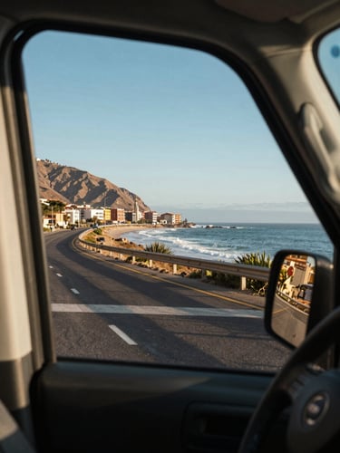 Medium shot from inside a van window looking out at the Chilean coastal road between Santiago and Viña del Mar, Pacific ocean visible in the distance under clear blue sky, warm afternoon light, landscape framed by the vehicle window edge