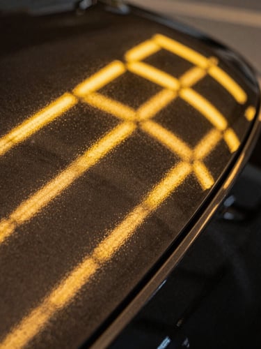 Extreme close-up of a flawless black car panel curve reflecting sharp, parallel yellow LED light-board lines with absolute straightness, showing perfect orange peel texture.