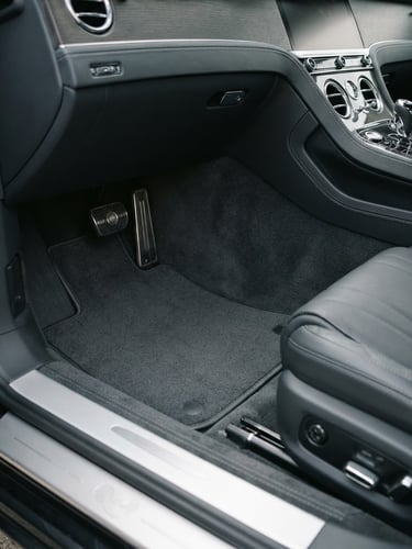 Wide panoramic luxury car interior footwell, dark grey tailored mat perfectly fitted, laser-cut edge detail visible, soft natural daylight, minimalist aesthetic, 35mm