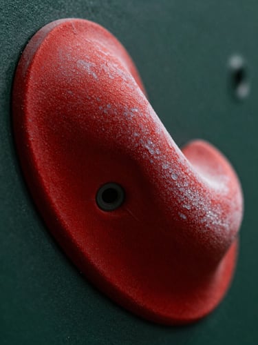 Macro shot of a vibrant crimson climbing hold showing rich dual-texture details, dramatic side-lighting emphasizing polyurethane friction.