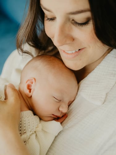 Bébé endormi contre sa maman souriante – photo naissance à domicile
