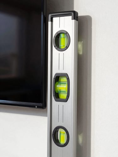 A close-up of a level being used on a newly mounted flat-screen TV on a clean wall, bright natural Florida sunlight, sharp focus on the level vial