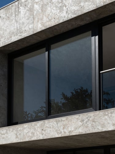 Sharp architectural photography of a modern concrete house facade in Mendoza with large black aluminum sliding window frames, strong directional sunlight, high-contrast shadows, 35mm lens