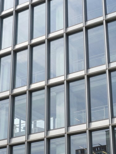 A modern commercial glass facade with clean aluminum frames, bright daylight reflecting off the energy-efficient glass, professional finish.