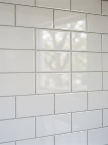 Close-up of a perfectly aligned, clean white subway tile backsplash in a bright Lansing kitchen, natural window light reflecting off the glossy glaze, neat grout lines, sharp focus, 35mm lens