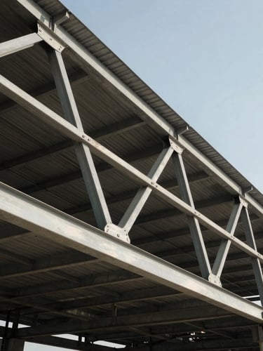 Low-angle heroic shot of massive PEB steel roof trusses mid-erection against a clear sky, harsh midday sun casting sharp shadows on raw steel