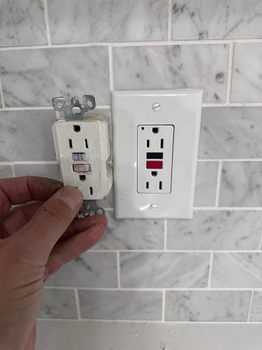 a person holding a white electrical outlet in a white tiled wall