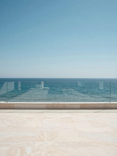 Wide environmental shot of a minimalist Costa del Sol terrace, frameless glass railing running along the edge, bright midday Mediterranean sun, the sea and sky filling the entire background beyond the glass, warm white stone floor in foreground, no people, architecture and horizon as subject, high contrast clarity