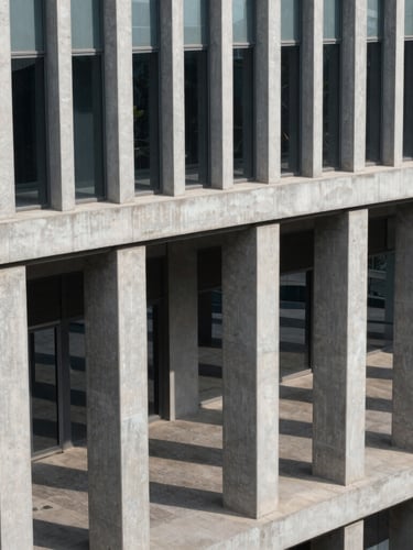 High-angle structured architectural view of modern concrete and steel columns in a clean Mumbai corporate headquarters, crisp daylight casting geometric shadows, no people.