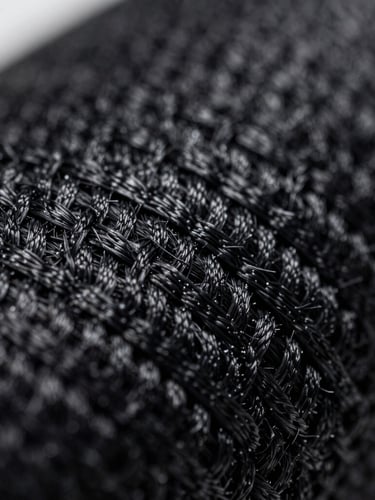 Extreme macro close-up of a raw technical textile weave, showing high-tensile black nylon fibers under sharp, high-contrast industrial lighting.