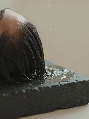 Macro shot of warm water flowing gently over dark hair on a black stone headrest, soft diffused natural light, shallow depth of field, 35mm