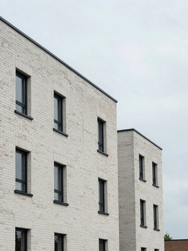 Clinical straight-on shot of a modern UK housing development under overcast daylight, clean slate brickwork, sharp architectural lines, negative space on the right.