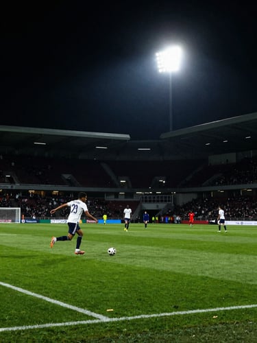 Dynamic sports photography, high-contrast stadium floodlights illuminating a green pitch, dramatic dark atmosphere, wide angle