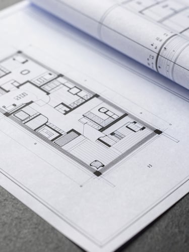 Close-up of architectural blueprints and clean financial ledgers on a slate surface, bright natural daylight, high-end editorial style