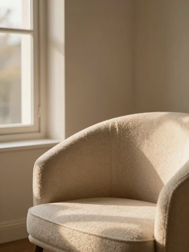 Close-up of a styled warm neutral living room corner with bouclé chair, golden-hour window light casting soft shadows, 35mm editorial photography