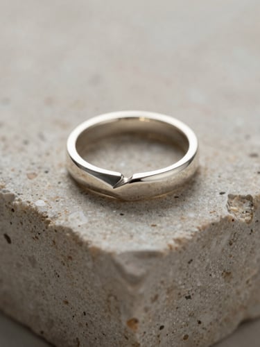 Extreme close-up macro shot of a minimalist geometric silver ring resting on a textured travertine stone block, soft natural side-light, elegant shadows, focus on metallic craftsmanship