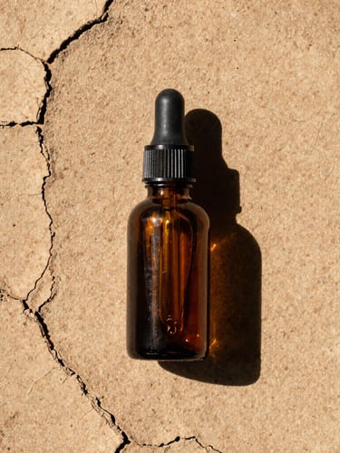 Overhead flat lay of amber glass dropper bottle on cracked earthy clay, harsh direct sunlight, sharp dark shadows, raw texture